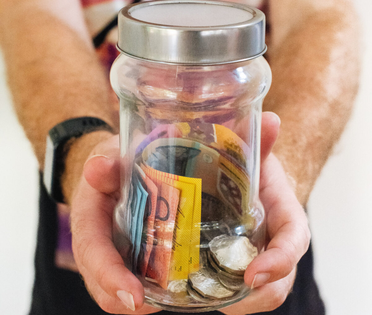 Australian bank notes in a glass jar being held