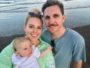 Parents Paige and Jordan holding their new born baby Nova on a beach