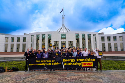 People holding banners outside the Parliament building in Canberra that read 'no worker or community left behind' and Energy transition Authority NOW'