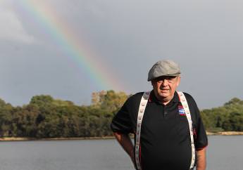Joe Mcdonald wearing braces and a flat cap with a rainbow in the background