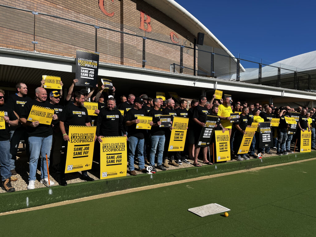 Group of Mining and Energy members stood on a lawn bowls lawn outside a bowling club holding Same Job Same Pay corflutes