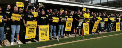 Group of Mining and Energy members stood on a lawn bowls lawn outside a bowling club holding Same Job Same Pay corflutes