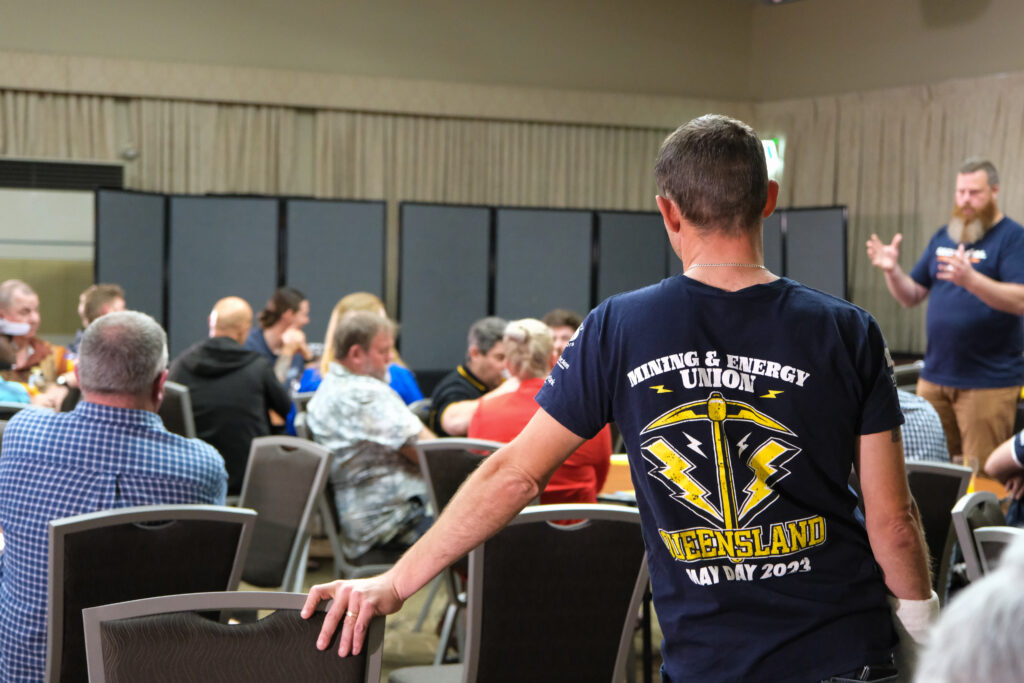 A group of people listening to Dan Repacholi speak on Same Job Same Pay. In the foreground is a member wearing an MEU Queensland May Day tshirt.