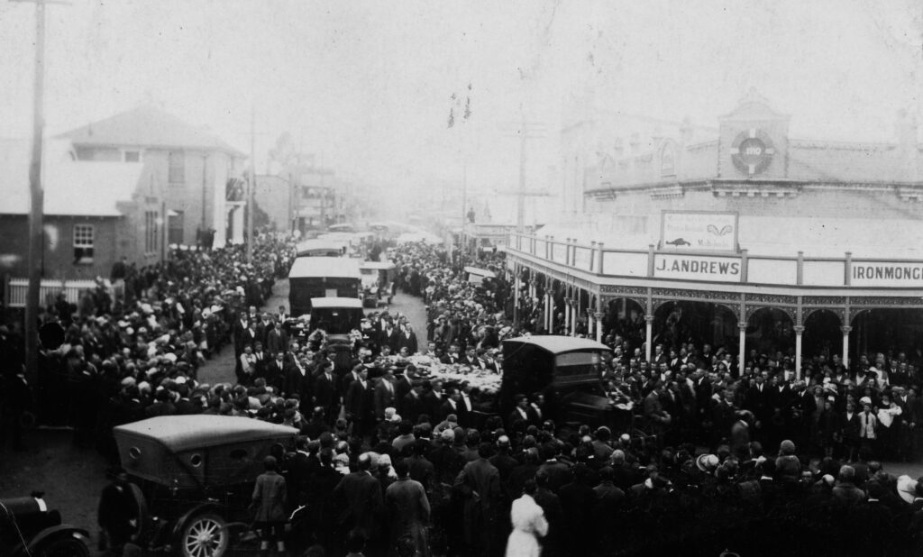 A black-and-white photo of the funeral procession for Bellbird victims. Thousands of onlookers crowd the street.