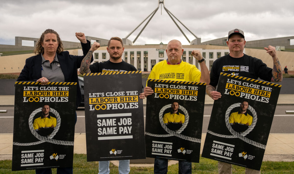 Four labour hire workers with raised fists holding same job same pay posters outside of Parliament House in Canberra